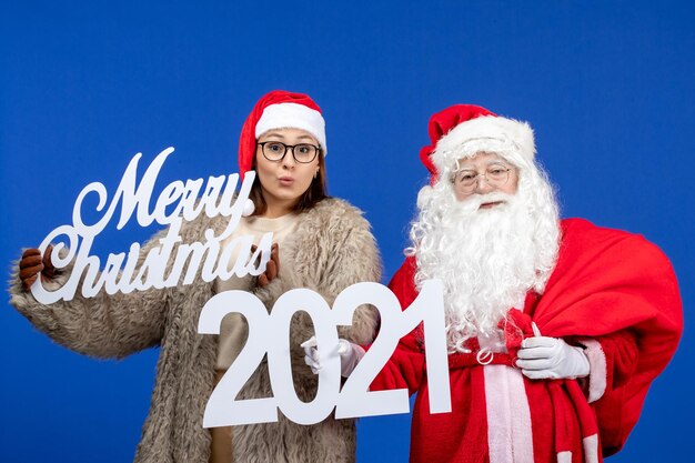 Vue de face du père noël avec une jeune femme tenant un joyeux noël et des écrits sur les vacances bleues