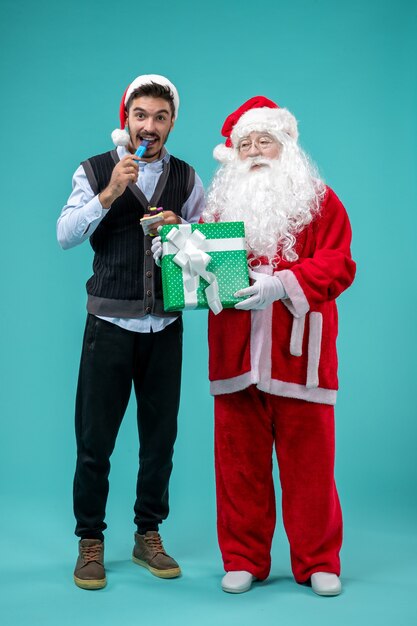 Vue de face du père Noël avec jeune homme et cadeau de vacances sur le mur bleu