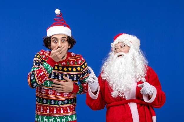 Vue de face du père noël avec un jeune homme sur le mur bleu