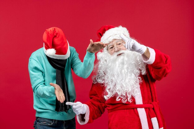 Vue de face du père noël avec un jeune homme sur un mur rouge