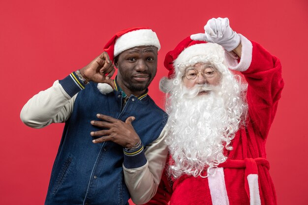 Vue de face du père Noël avec jeune homme sur mur rouge