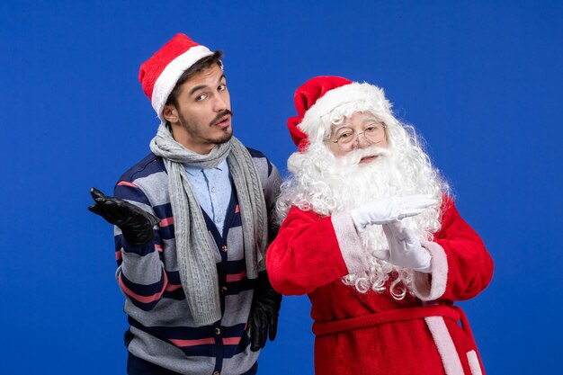 Vue de face du père noël avec un jeune homme posant sur le mur bleu