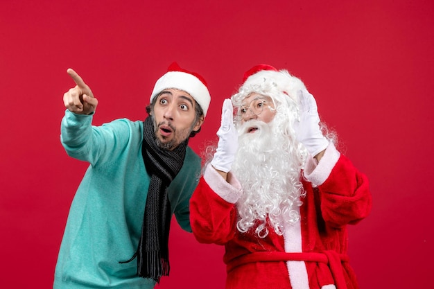 Vue de face du père noël avec un jeune homme posant sur le mur rouge