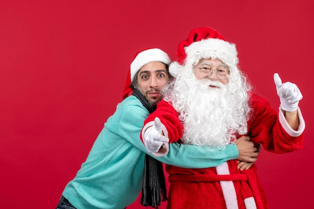 Vue de face du père noël avec un jeune homme posant sur le mur rouge