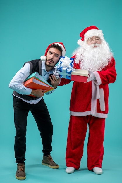 Vue de face du père Noël avec jeune homme et présente sur mur bleu