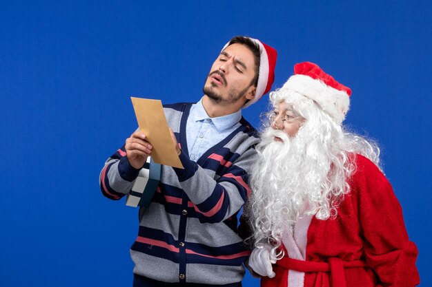 Vue de face du père noël avec un jeune homme qui lit une lettre sur le mur bleu