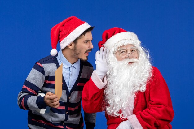 Vue de face du père noël avec un jeune homme qui tient une lettre sur le mur bleu