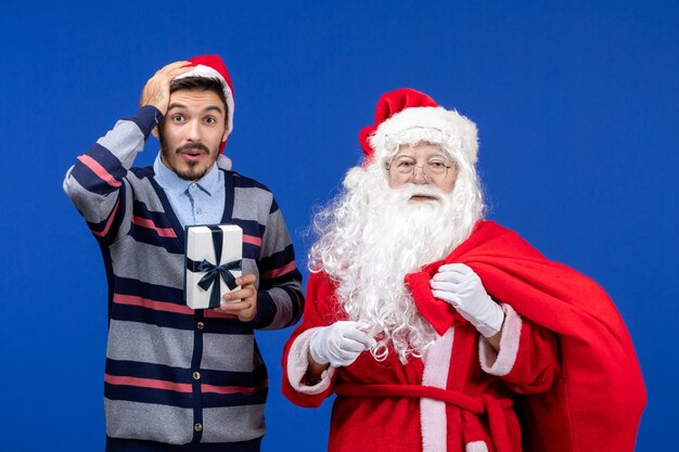 Vue de face du père noël avec un jeune homme sac de transport plein de cadeaux sur l'émotion bleue présente noël