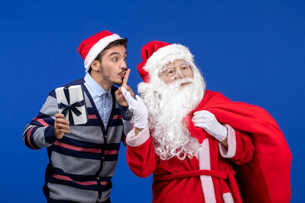 Vue de face du père noël avec un jeune homme sac de transport plein de cadeaux sur les vacances d'émotion bleue présente noël