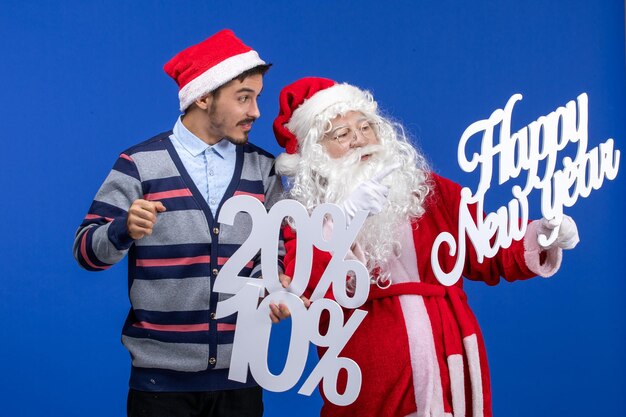 Vue de face du père noël avec un jeune homme tenant une bonne année et des écrits en pourcentage sur le mur bleu