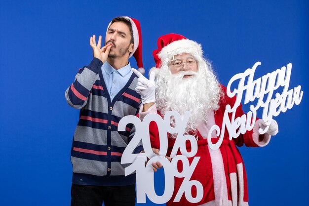 Vue de face du père noël avec un jeune homme tenant une bonne année et des écrits en pourcentage sur le mur bleu