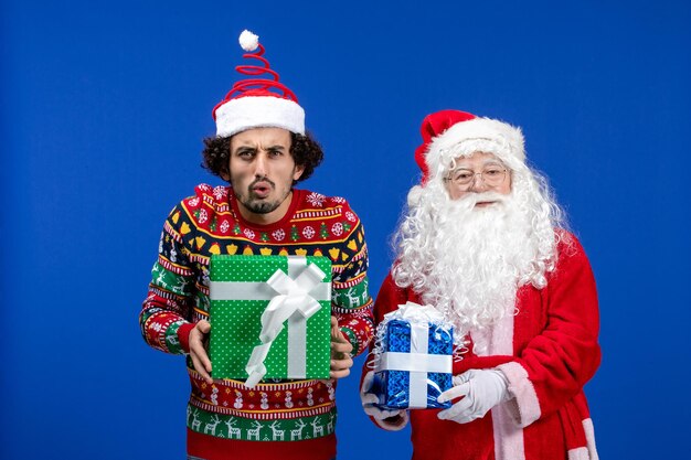 Vue de face du père noël avec un jeune homme tenant des cadeaux de noël sur le mur bleu