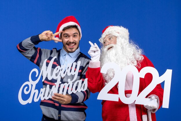 Vue de face du père noël avec un jeune homme tenant et joyeux noël écrits sur bleu