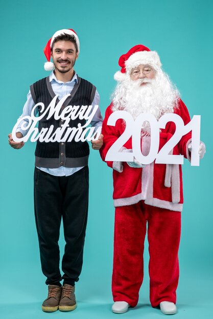 Vue de face du père Noël avec jeune homme tenant joyeux Noël et écritures sur le fond bleu