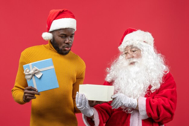 Vue de face du père Noël avec jeune homme tenant présent sur le mur rouge