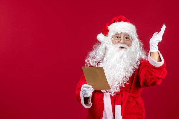 Vue de face du père noël lisant la lettre d'un enfant sur le rouge présente l'émotion des vacances de noël