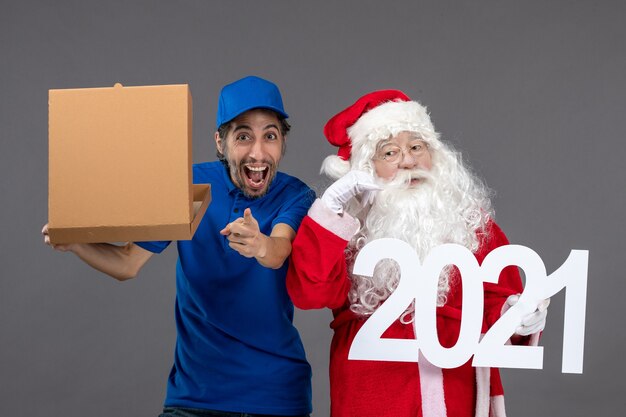 Vue de face du père noël avec messager mâle tenant une boîte de nourriture et écrit sur le mur gris