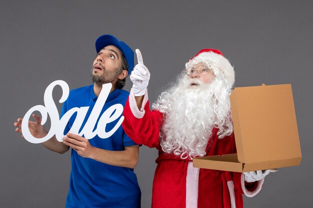 Vue de face du père noël avec messager masculin holding vente écrit et boîte de nourriture sur mur gris