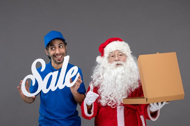 Photo gratuite vue de face du père noël avec messager masculin tenant la bannière de vente et les boîtes de nourriture sur le mur gris