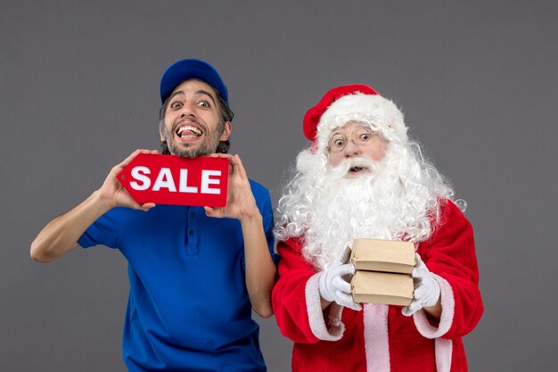 Vue de face du père Noël avec messager masculin tenant la bannière de vente et les emballages alimentaires sur le mur gris