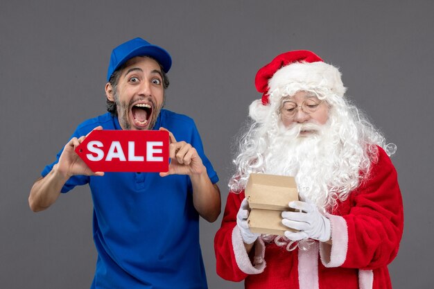 Vue de face du père Noël avec messager masculin tenant la bannière de vente et les emballages alimentaires sur le mur gris