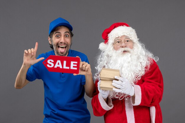 Vue de face du père Noël avec messager masculin tenant la bannière de vente et les emballages alimentaires sur le mur gris