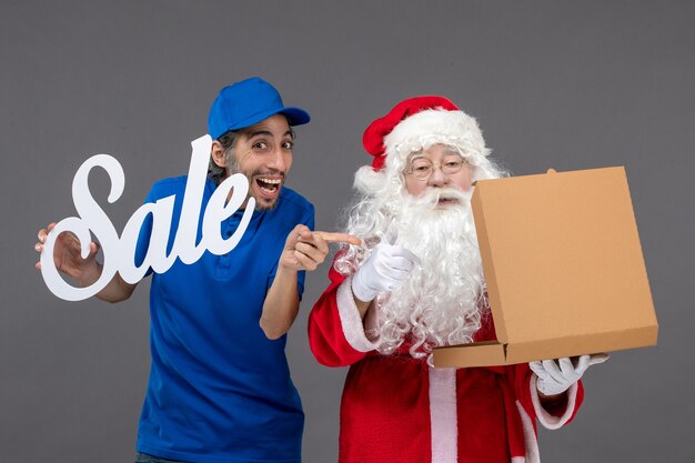 Vue de face du père Noël avec messager masculin tenant la bannière de vente et l'ouverture de la boîte de nourriture sur le mur gris