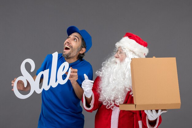 Vue de face du père Noël avec messager masculin tenant la bannière de vente et l'ouverture de la boîte de nourriture sur le mur gris