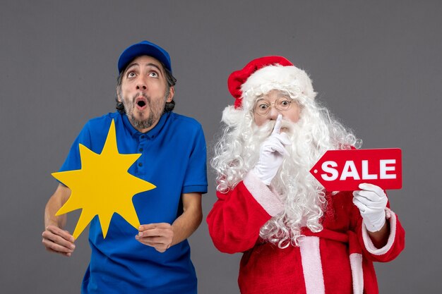 Vue de face du père Noël avec messager masculin tenant la bannière de vente et panneau jaune sur le mur gris