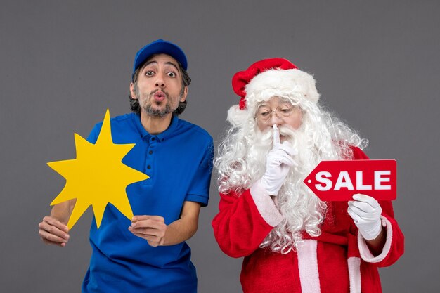 Vue de face du père Noël avec messager masculin tenant la bannière de vente et panneau jaune sur le mur gris