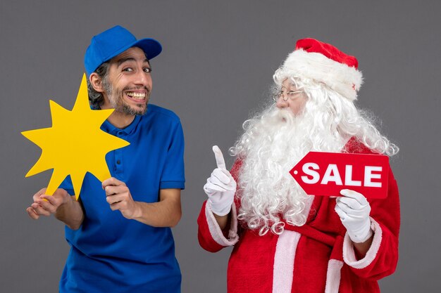 Vue de face du père Noël avec messager masculin tenant la bannière de vente et panneau jaune sur le mur gris