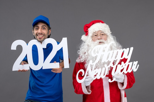 Vue de face du père Noël avec messager masculin tenant bonne année et planches 2021 sur le mur gris