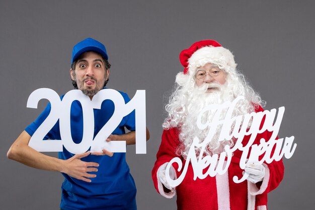 Vue de face du père Noël avec messager masculin tenant bonne année et planches 2021 sur le mur gris