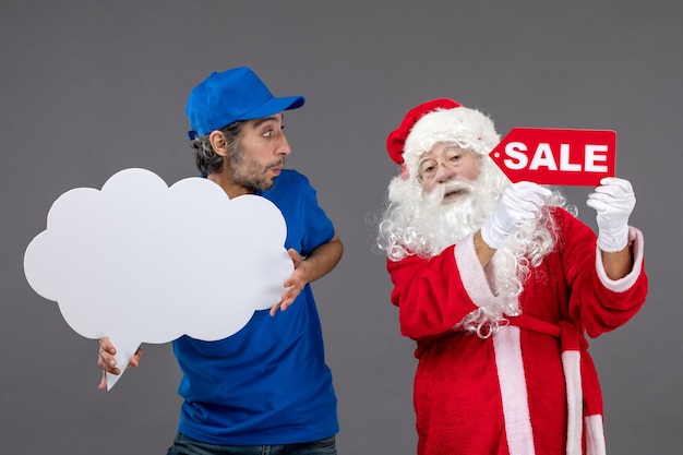 Photo gratuite vue de face du père noël avec messager masculin tenant l'écriture de vente et signe de nuage sur le mur gris