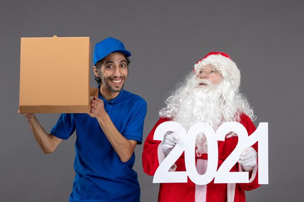 Vue de face du père Noël avec messager masculin tenant des sacs à provisions et une boîte de nourriture sur le mur gris