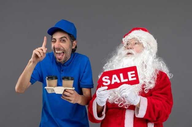 Vue de face du père noël avec messager masculin tenant vente écrit et café sur mur gris