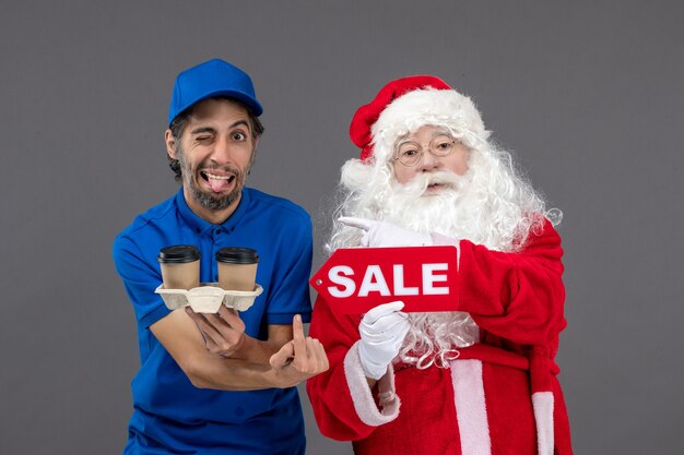 Vue de face du père noël avec messager masculin tenant vente écrit et café sur mur gris