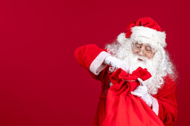 Vue de face du père noël ouvrant un sac rouge plein de cadeaux pour les enfants en vacances rouges émotions de noël