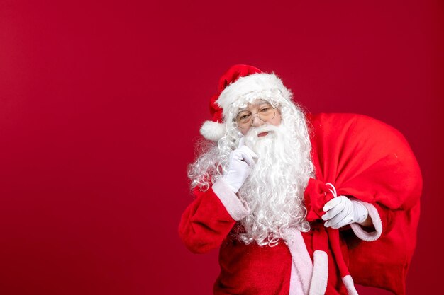 Vue de face du père noël portant un sac rouge plein de cadeaux sur les émotions rouges vacances de noël du nouvel an