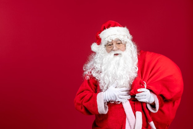 Vue de face du père noël portant un sac rouge plein de cadeaux sur le sol rouge émotion de noël nouvel an