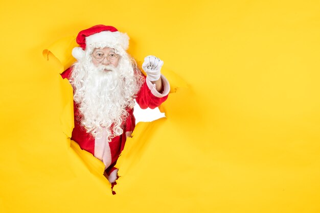 Vue de face du père Noël à la recherche à travers le mur jaune de papier déchiré