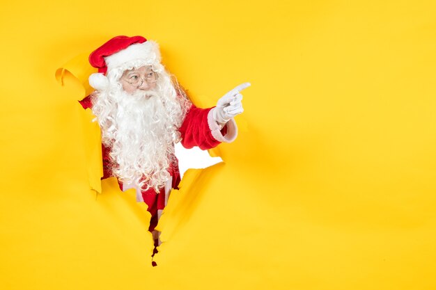 Vue de face du père Noël à la recherche à travers le mur jaune de papier déchiré