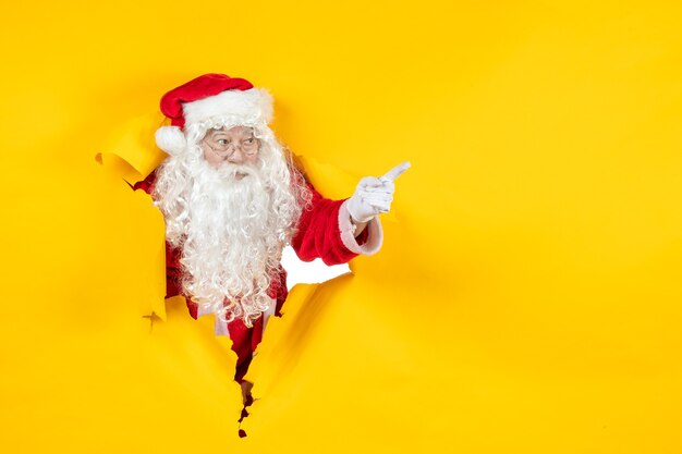 Vue de face du père Noël à la recherche à travers le mur jaune de papier déchiré