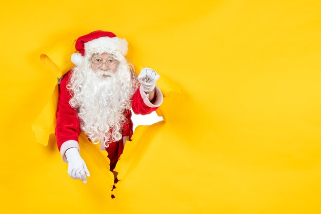 Vue de face du père Noël à la recherche à travers le mur jaune de papier déchiré