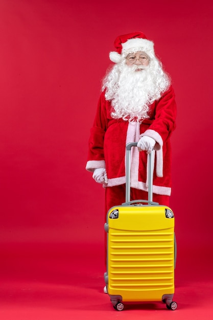 Vue de face du père Noël avec sac jaune préparation pour voyage sur mur rouge