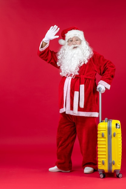 Vue de face du père Noël avec sac jaune préparation pour voyage sur mur rouge