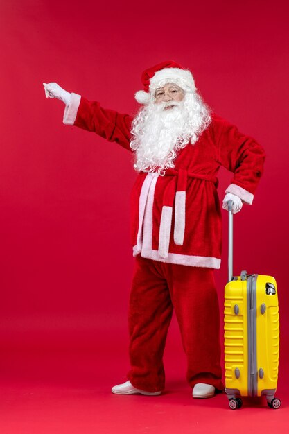 Vue de face du père Noël avec sac jaune préparation pour voyage sur mur rouge