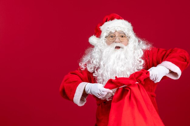 Vue de face du père noël sac d'ouverture plein de cadeaux pour les enfants sur le sol rouge vacances noël émotion