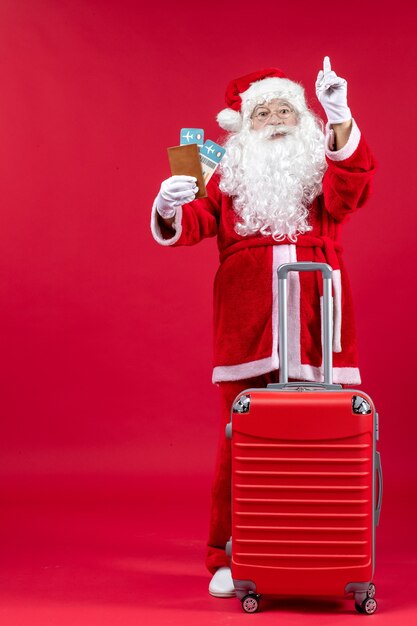 Vue de face du père Noël avec sac tenant des billets et se préparant pour le voyage sur le mur rouge