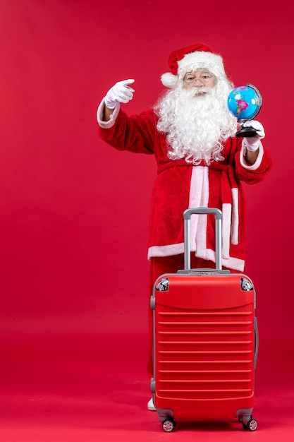 Vue de face du père Noël avec sac tenant le globe et préparation pour le voyage sur le mur rouge